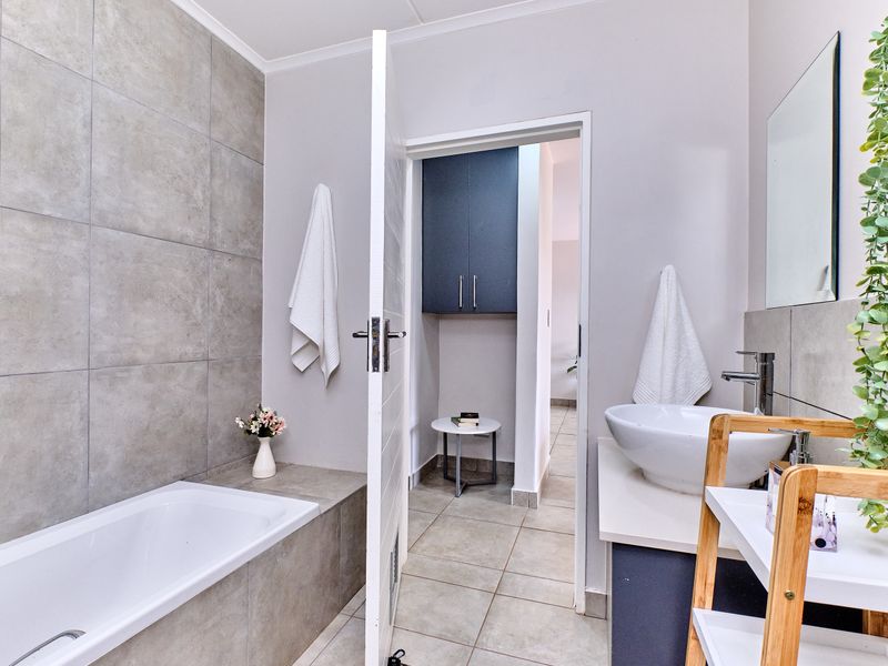 Modern bathroom featuring a built-in bathtub with grey tile surround, a vessel sink on a vanity cabinet, and additional built-in storage.