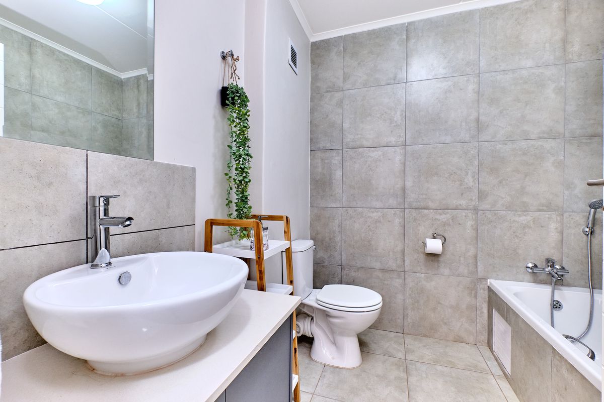 Modern bathroom featuring a vessel sink, vanity cabinet, toilet, and a bathtub with a handheld shower head, finished with neutral ceramic tiling.