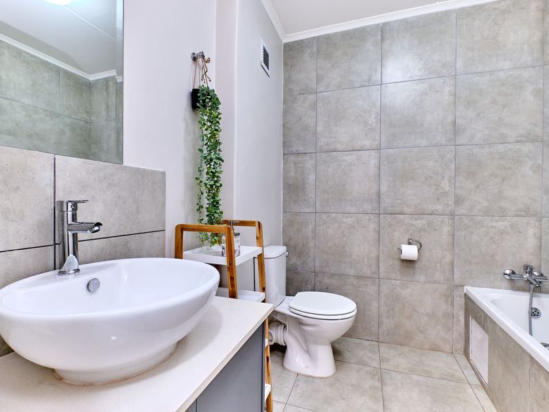 Modern bathroom featuring a vessel sink, vanity cabinet, toilet, and a bathtub with a handheld shower head, finished with neutral ceramic tiling.