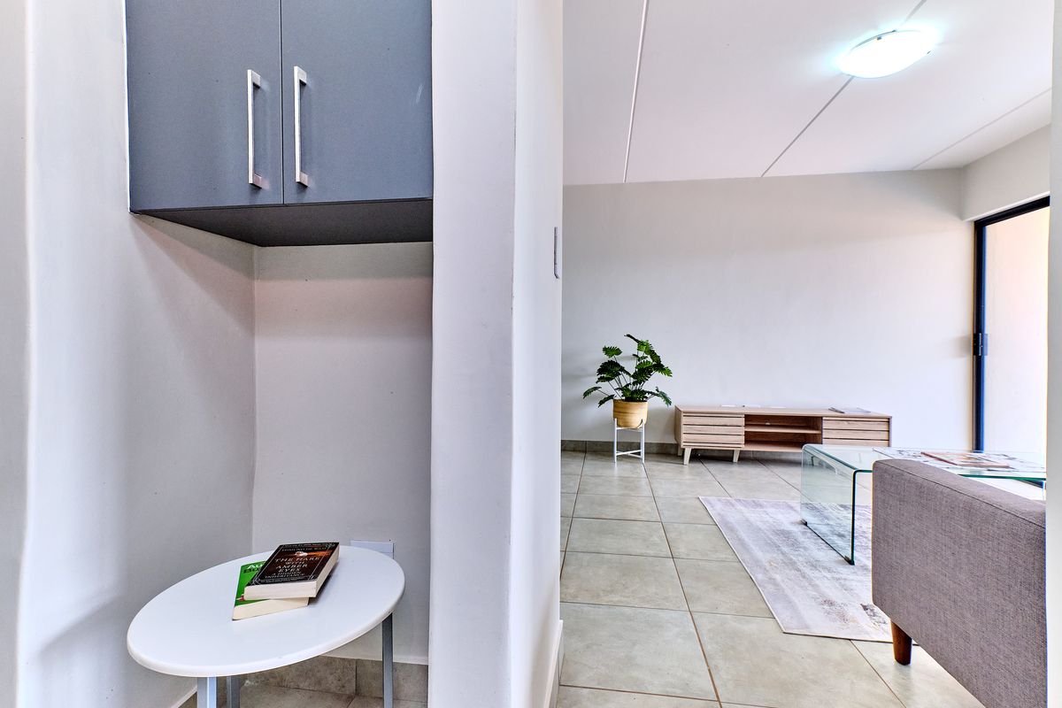 A bright living area featuring neutral tiled flooring and built-in overhead storage cabinetry, offering a clean and functional space.