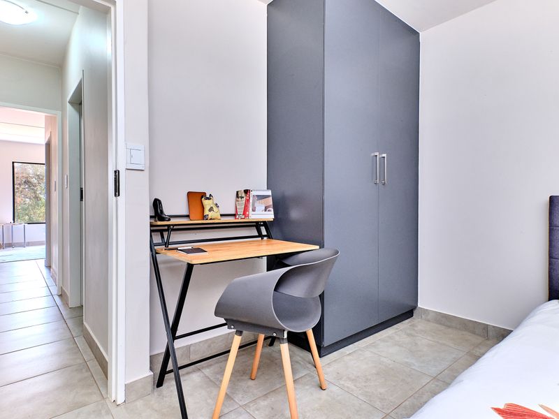 A bedroom featuring a built-in grey wardrobe and tiled flooring, with an adjacent hallway view.