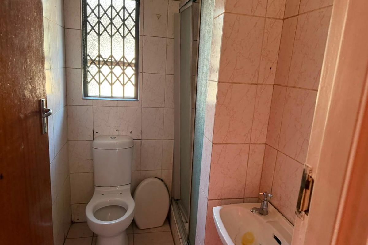 A compact bathroom featuring a shower enclosure, toilet, and wall-mounted basin with tiled finishes throughout.