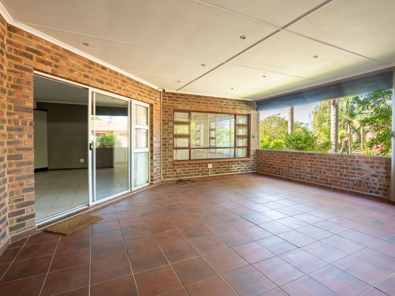 A spacious covered patio featuring exposed brick walls, tiled flooring, and sliding glass doors leading into the interior living area.