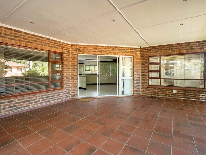 A spacious covered patio featuring exposed brick walls, tiled flooring, and large windows, providing a seamless transition to the interior living space.