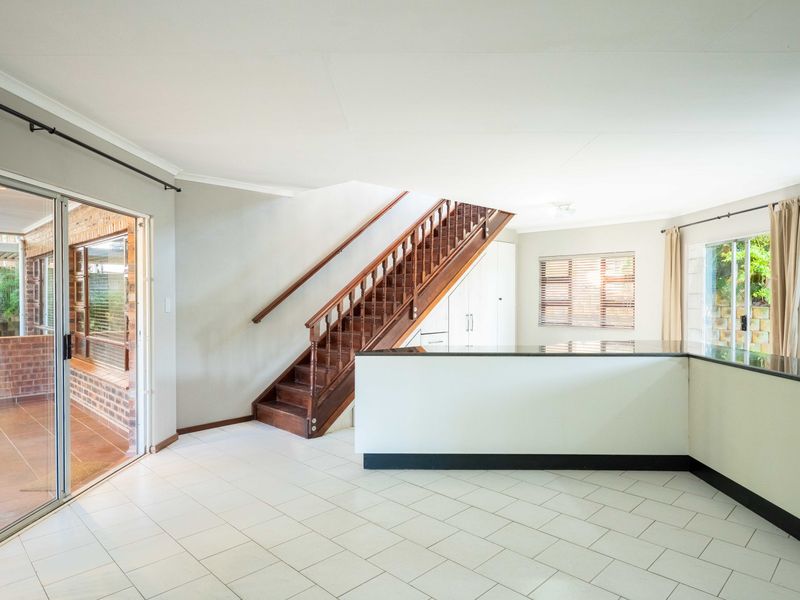 Spacious open-plan living area featuring a wooden staircase, tiled flooring, and a breakfast bar with granite countertops, leading out to a covered patio.
