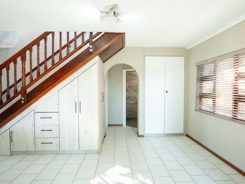 A bright hallway featuring a wooden staircase with integrated under-stair storage, tiled flooring, and built-in cupboard space.