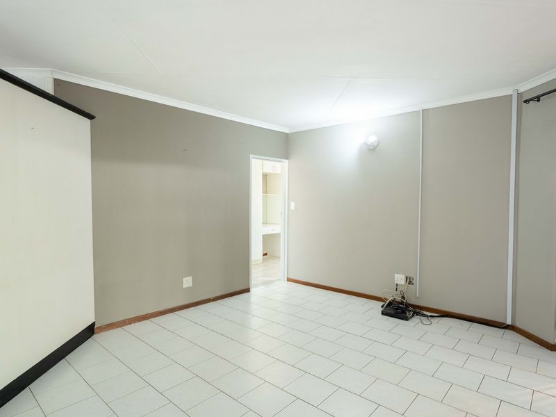 An empty living room featuring neutral wall tones and tiled flooring, with a doorway leading to an adjacent utility or kitchen area.