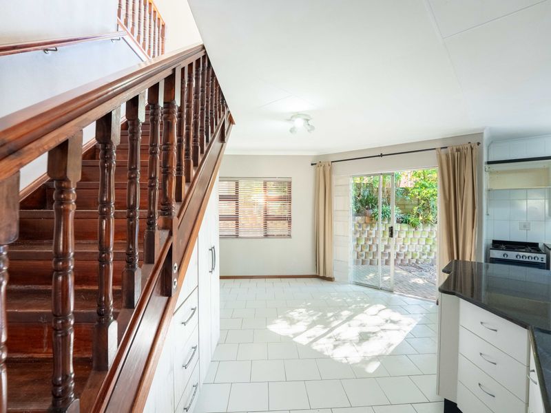 Open plan living and kitchen area featuring a wooden staircase, tiled flooring, and direct access to the rear patio through sliding glass doors.