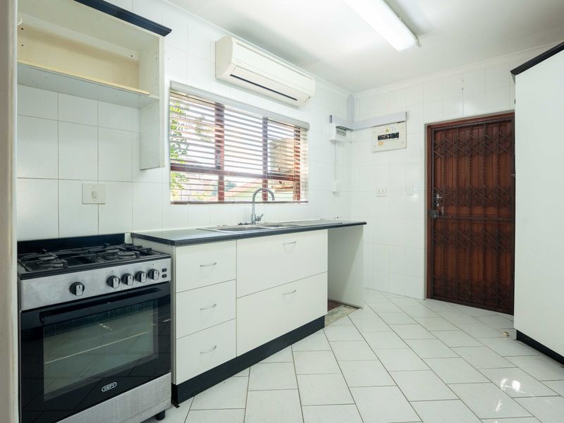 A functional kitchen featuring white cabinetry, a gas stove with oven, tiled surfaces, and a security gate leading to the exterior.