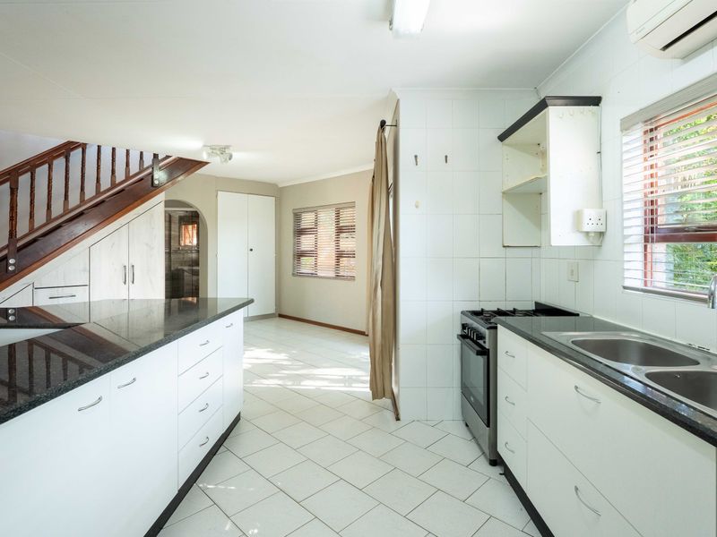 A functional kitchen featuring granite countertops, white cabinetry, a gas stove, and tiled flooring, with an adjacent staircase and open-plan layout.