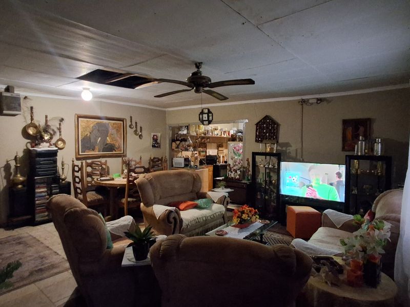 Open-plan living and dining area featuring tiled floors and a ceiling fan, requiring maintenance to the ceiling and general interior updates.