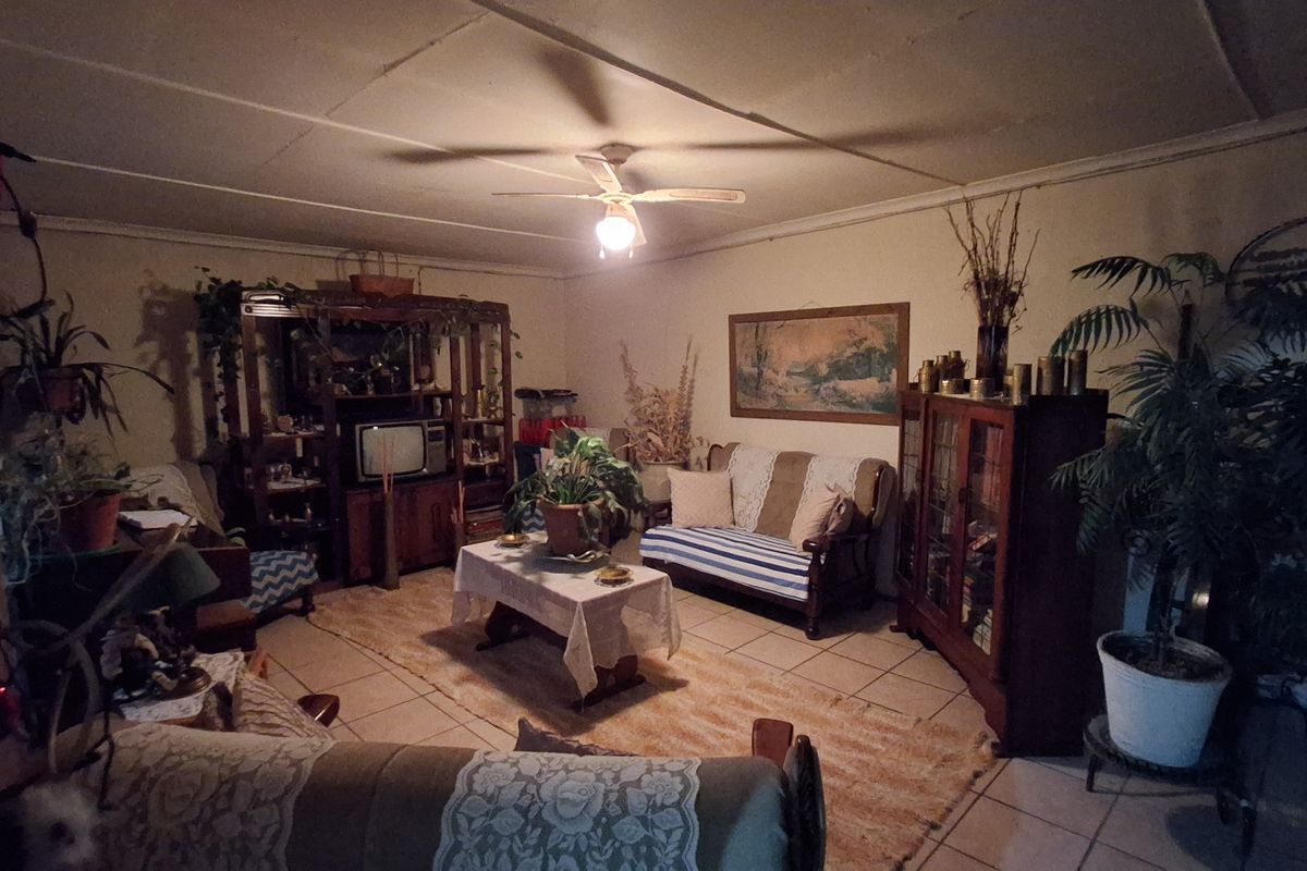 A living room featuring tiled flooring and a ceiling fan, currently presented with dated finishes and low-light conditions.