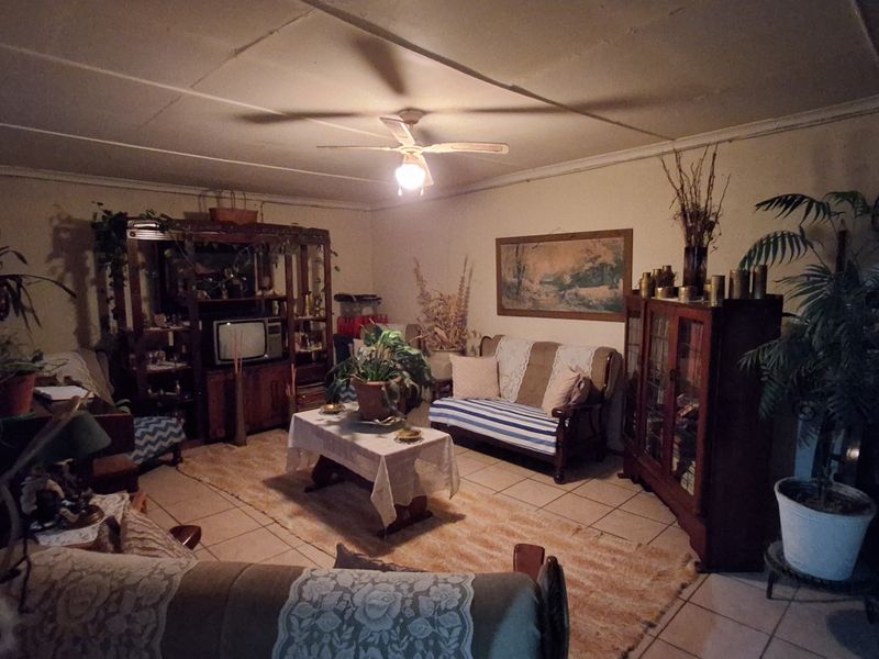 A living room featuring tiled flooring and a ceiling fan, currently presented with dated finishes and low-light conditions.
