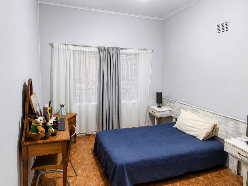 A functional bedroom featuring a built-in headboard, neutral wall finishes, and tiled flooring, offering a comfortable and well-lit space.