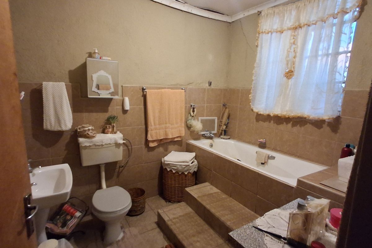 A dated bathroom featuring a pedestal basin, toilet, and a tiled bathtub surround with steps, requiring cosmetic updates to improve its overall condition.