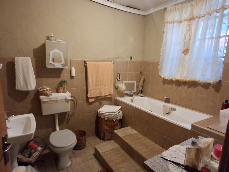 A dated bathroom featuring a pedestal basin, toilet, and a tiled bathtub surround with steps, requiring cosmetic updates to improve its overall condition.