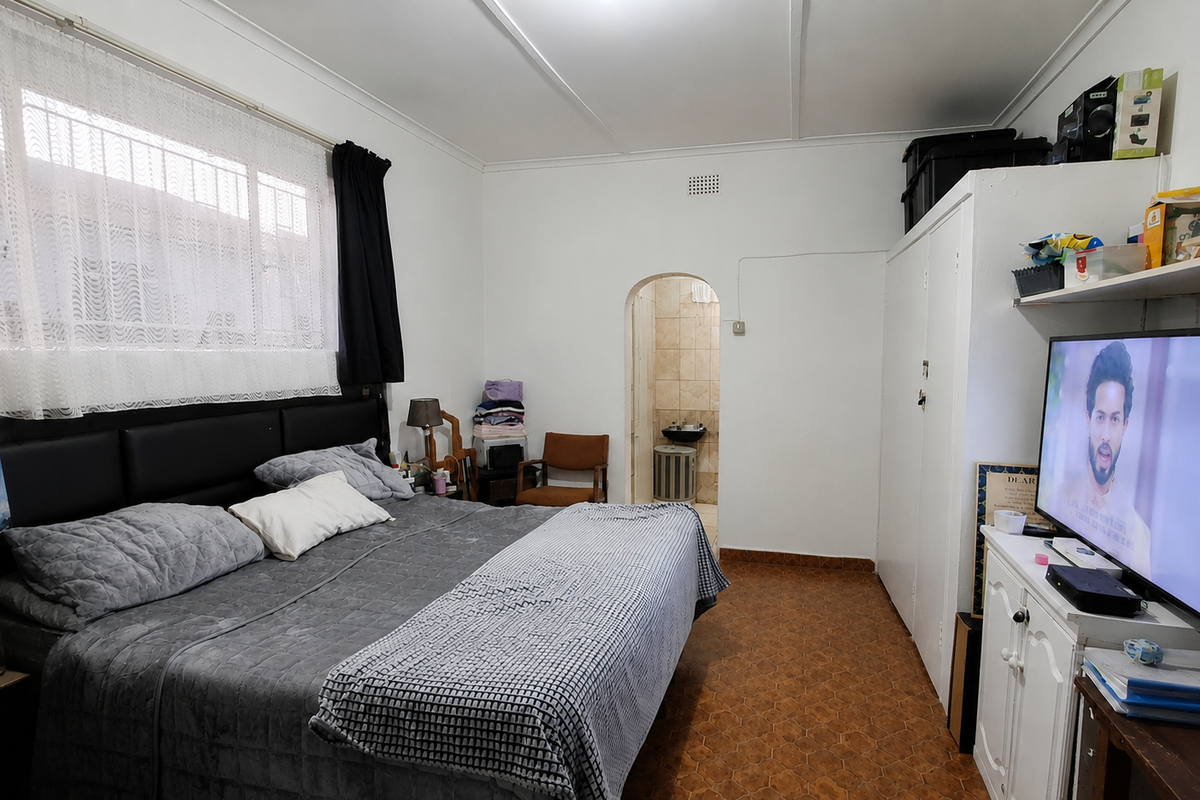 A bedroom featuring built-in wardrobe storage, an arched doorway leading to an en-suite, and tiled flooring throughout.