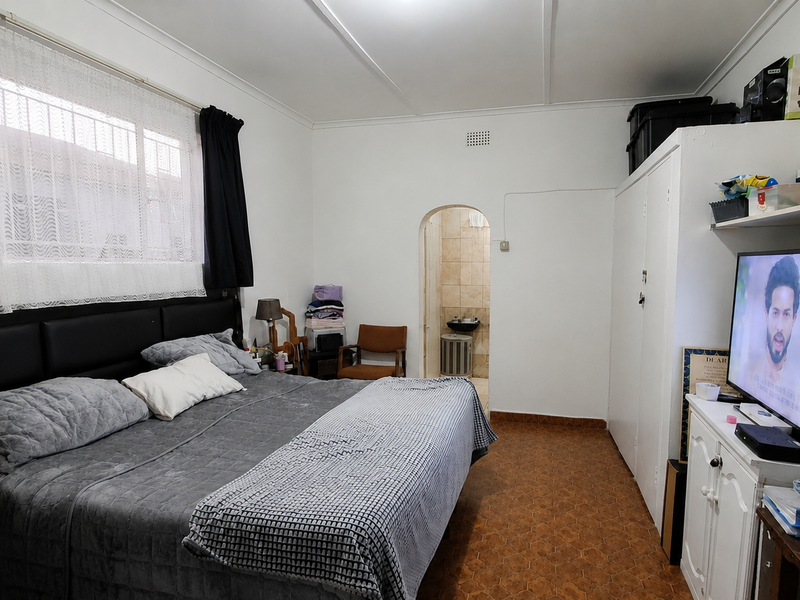 A bedroom featuring built-in wardrobe storage, an arched doorway leading to an en-suite, and tiled flooring throughout.