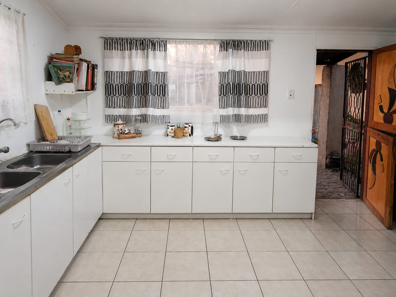 A functional kitchen featuring white cabinetry, laminate countertops, a double stainless steel sink, and ceramic floor tiles, with a unique wooden stable door.