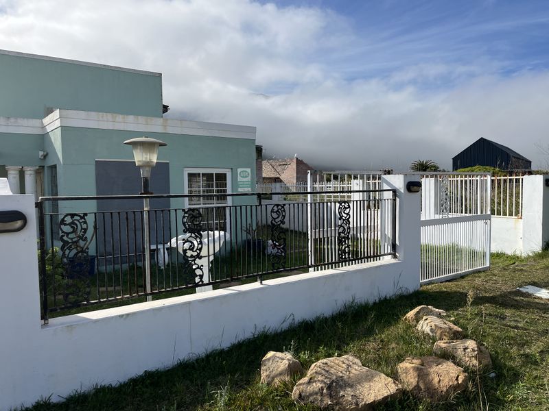 Front exterior view of the property featuring a masonry boundary wall, wrought iron fencing, and gated access with visible signs of weathering.