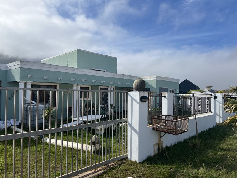 Front elevation of a single-story house featuring a masonry boundary wall, metal fencing, and concrete columns with visible exterior wear.