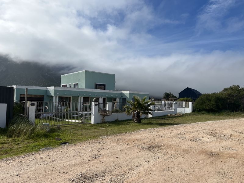 Front exterior view of a detached house featuring a gated entrance, perimeter fencing, and a flat roof design set against a mountain backdrop.