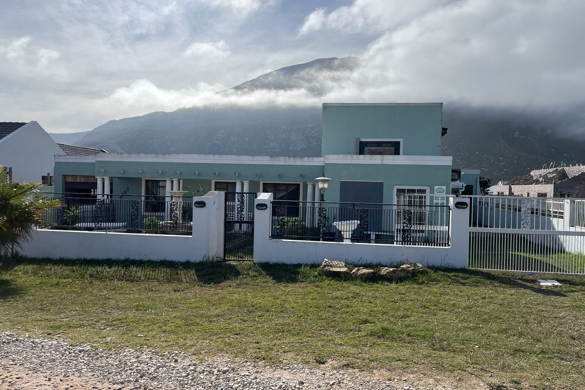 Front elevation of a detached house featuring a boundary wall, wrought iron fencing, and a paved driveway with mountain views in the background.
