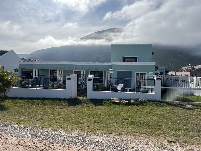 Front elevation of a detached house featuring a boundary wall, wrought iron fencing, and a paved driveway with mountain views in the background.