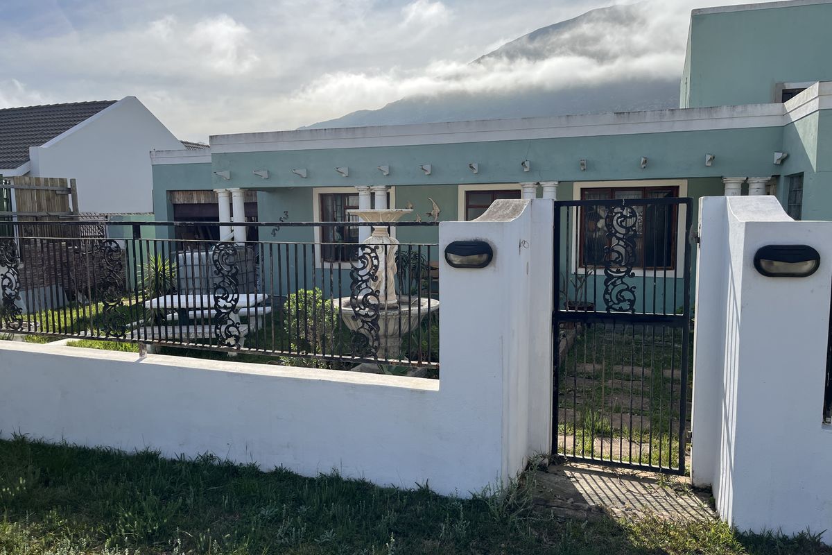 Front elevation of a house featuring a gated entrance, a covered patio area, and a mountain backdrop.