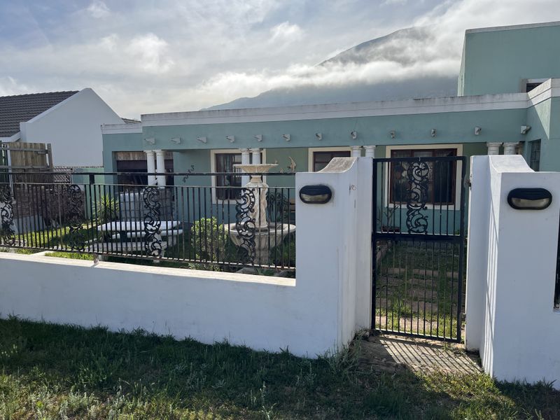 Front elevation of a house featuring a gated entrance, a covered patio area, and a mountain backdrop.