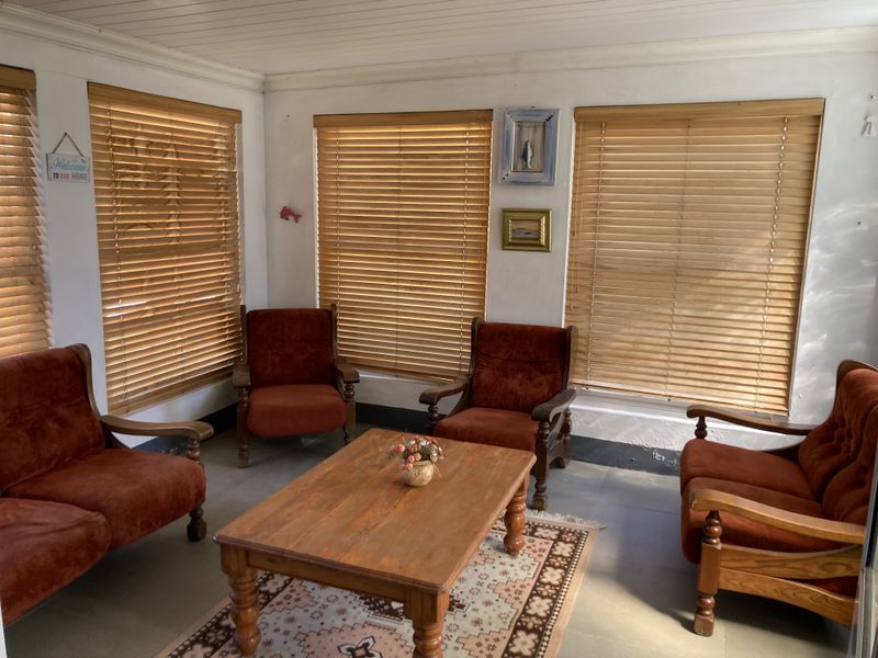 A sunlit living area featuring tiled flooring, tongue and groove ceiling, and wooden venetian blinds on multiple windows.