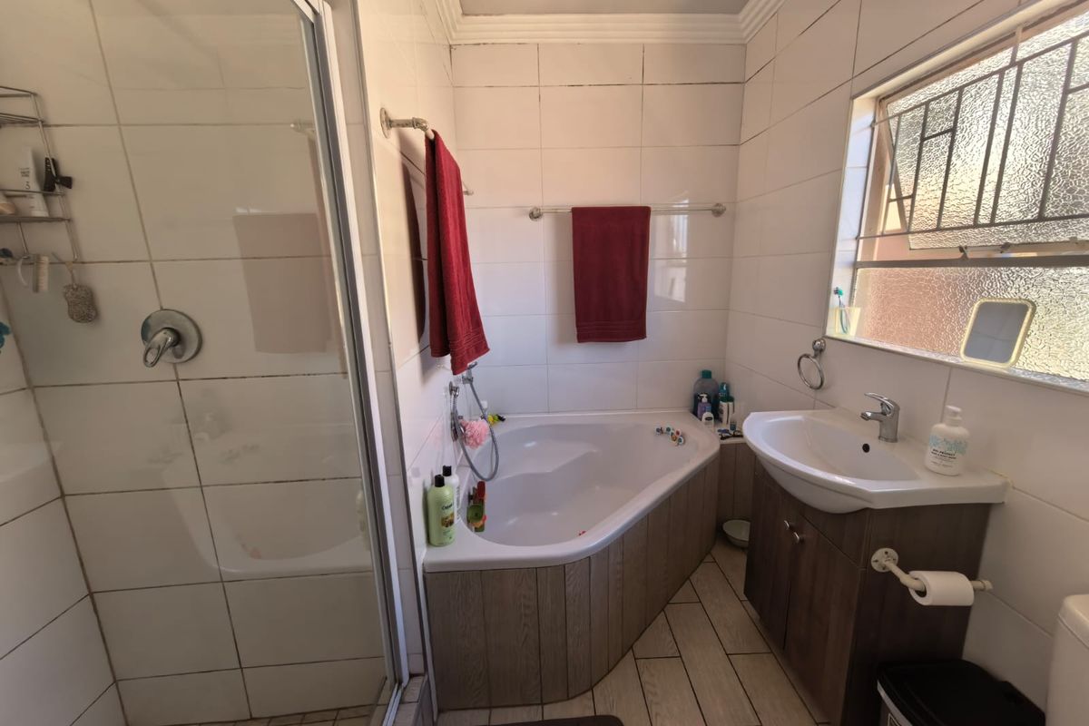 A functional bathroom featuring a corner bathtub, separate shower enclosure, and a vanity basin with tiled finishes throughout.