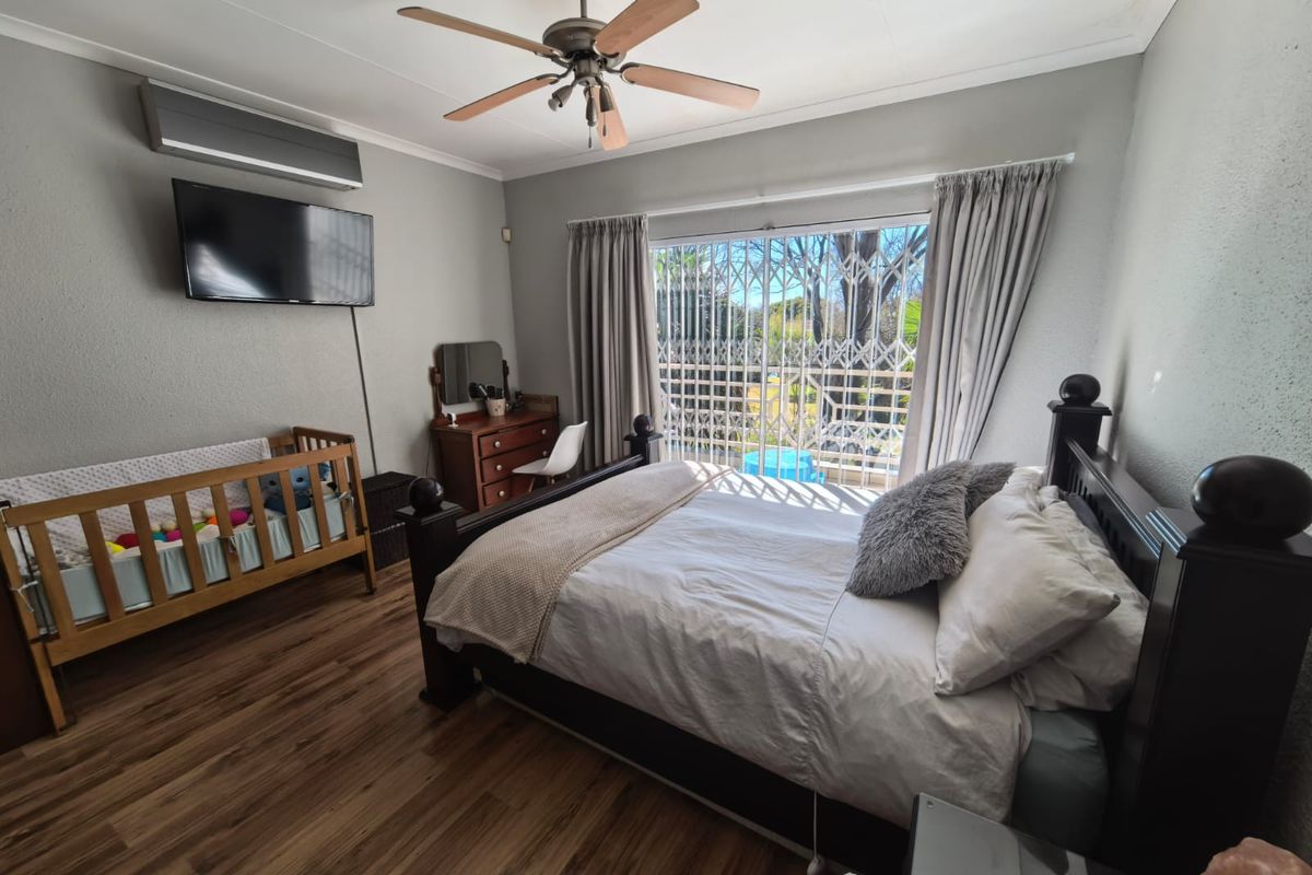A well-lit bedroom featuring laminate flooring, a ceiling fan, and a split-system air conditioner, with direct access to the outdoors via a sliding glass door.