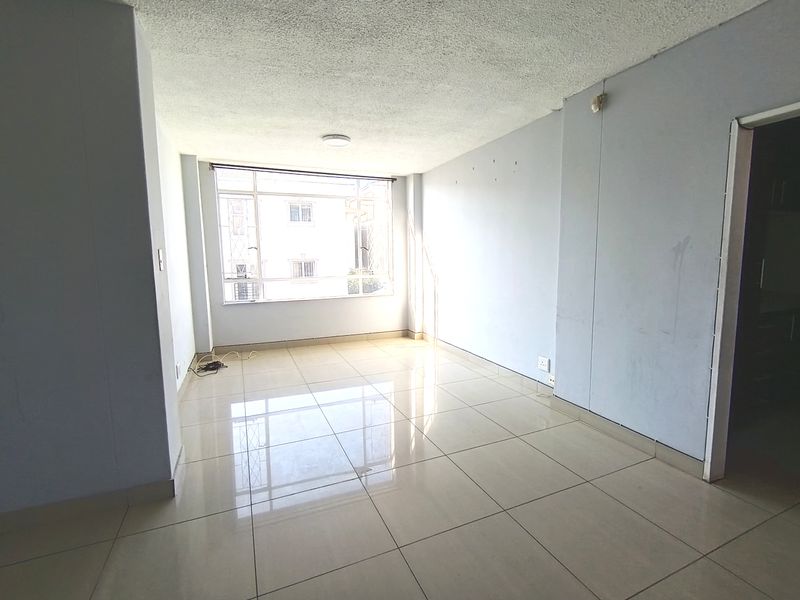 An empty, sunlit living area featuring neutral tiled flooring, large windows, and textured ceilings, ready for personalization.