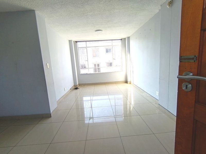 An empty, sunlit living room featuring large windows and tiled flooring, ready for renovation or staging.