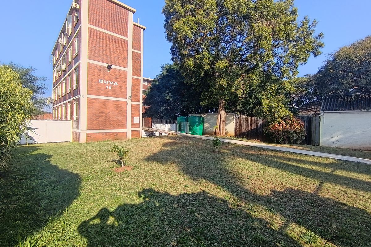 Rear view of the apartment building showing a communal lawn area, paved pathway, and water storage tanks.