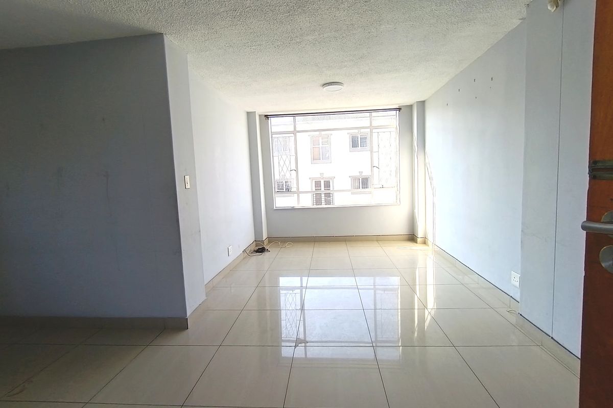 An empty, well-lit living area featuring neutral tiled flooring and a large window, providing a blank canvas for interior design.
