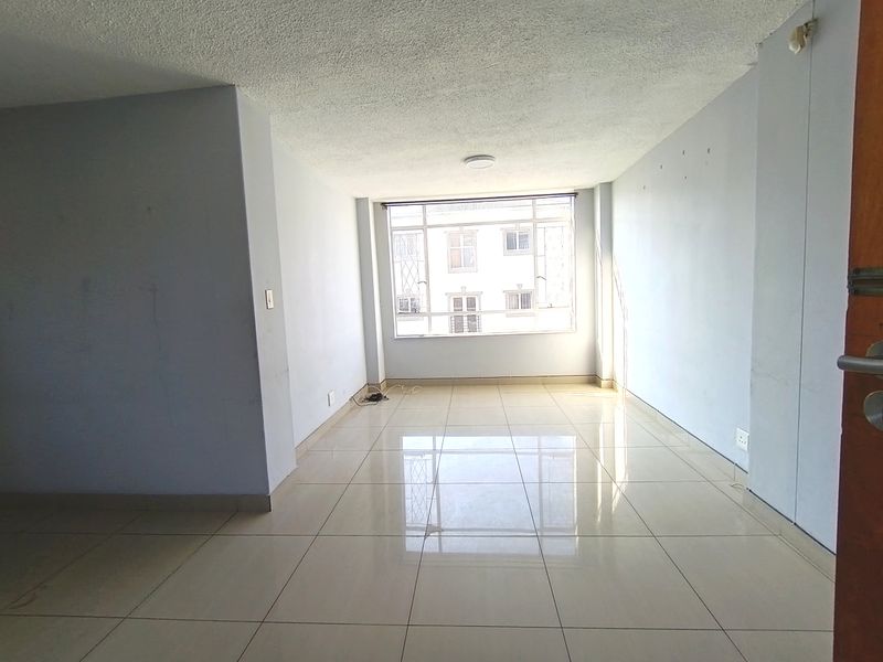 An empty, well-lit living area featuring neutral tiled flooring and a large window, providing a blank canvas for interior design.