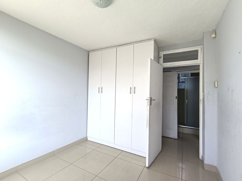 A vacant bedroom featuring neutral tiled flooring, built-in white cupboards, and direct access to an adjoining room.