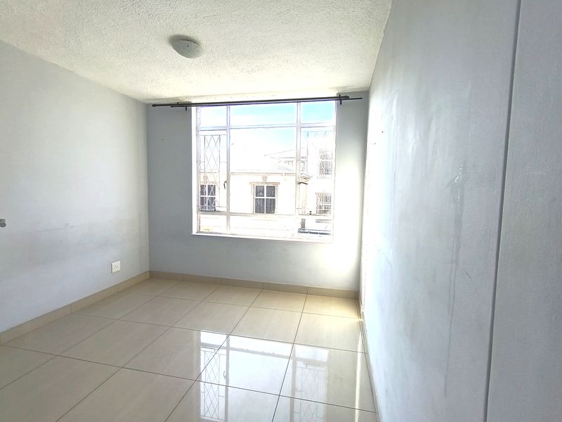 An empty bedroom featuring tiled flooring, a large window with security bars, and neutral walls, offering a blank canvas for personalization.