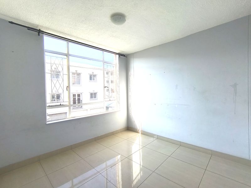 An empty bedroom featuring tiled flooring, a large window with security bars, and a neutral wall finish.