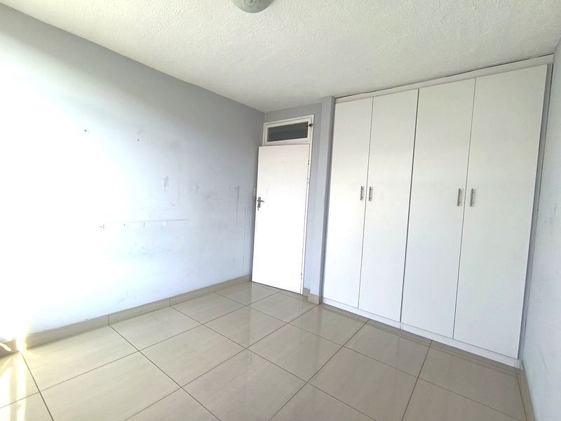 An empty bedroom featuring neutral tiled flooring, built-in white cupboards, and a standard door with a transom window above.
