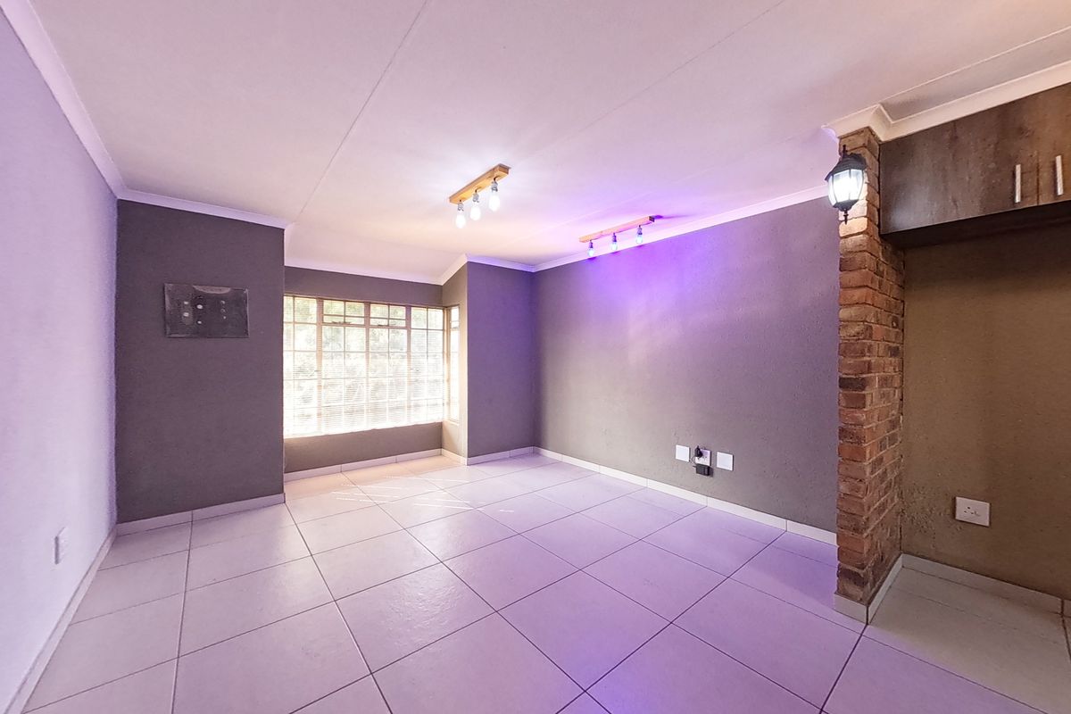A spacious, empty living area featuring neutral tiled flooring, an exposed brick feature pillar, and modern ceiling lighting, offering a versatile blank canvas.