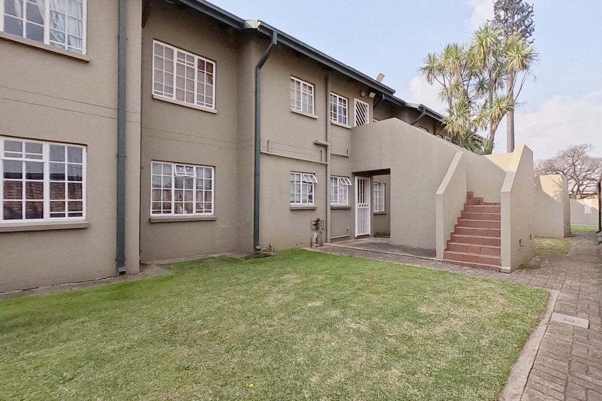 Rear view of the townhouse complex featuring a communal lawn, paved walkway, and an external staircase leading to upper-level units.