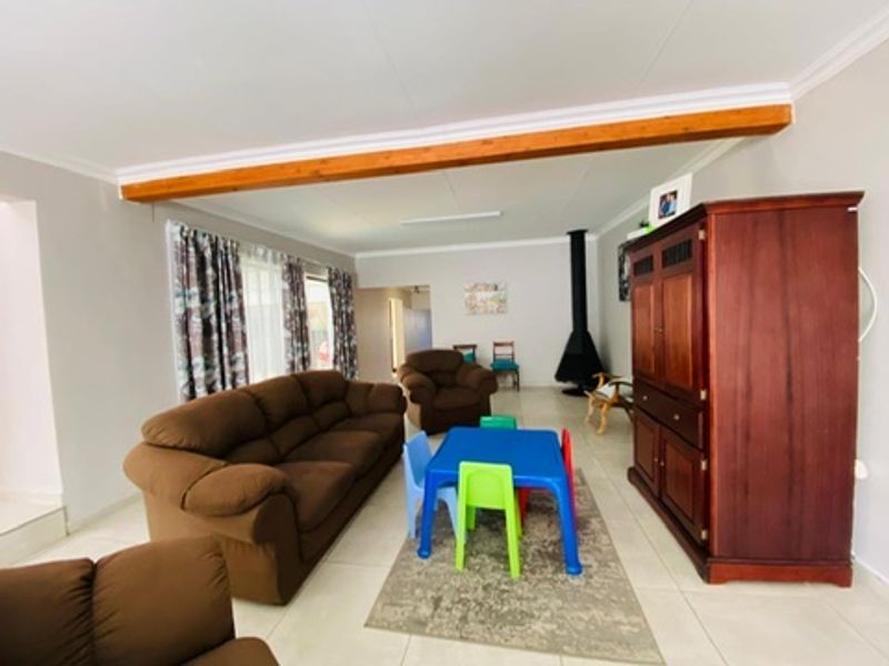 Spacious living room featuring a prominent exposed timber ceiling beam, tiled flooring, and a freestanding fireplace, offering a comfortable and functional family space.