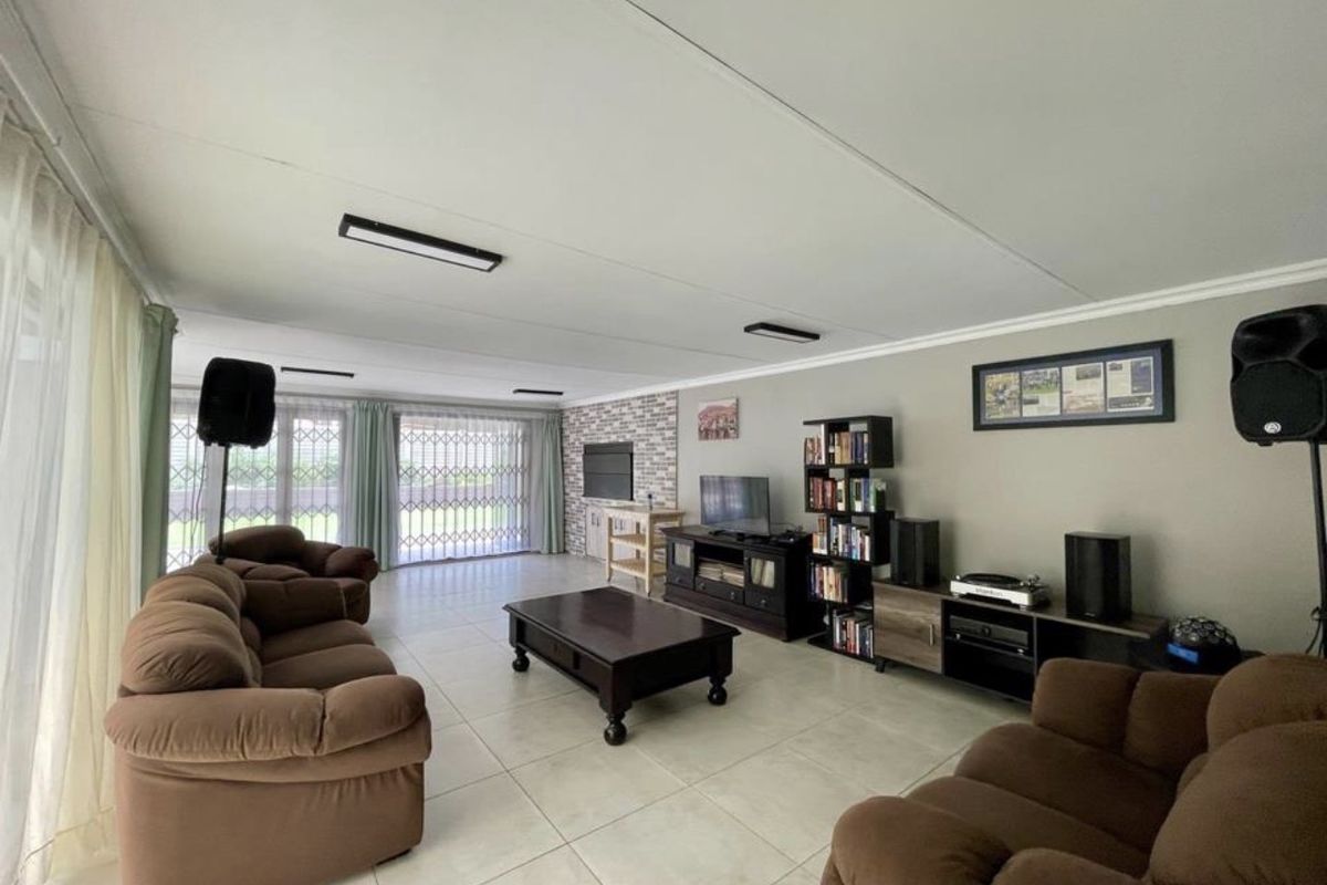 Spacious living room featuring large format floor tiles, a brick feature wall, and sliding glass doors with security gates leading to the exterior.