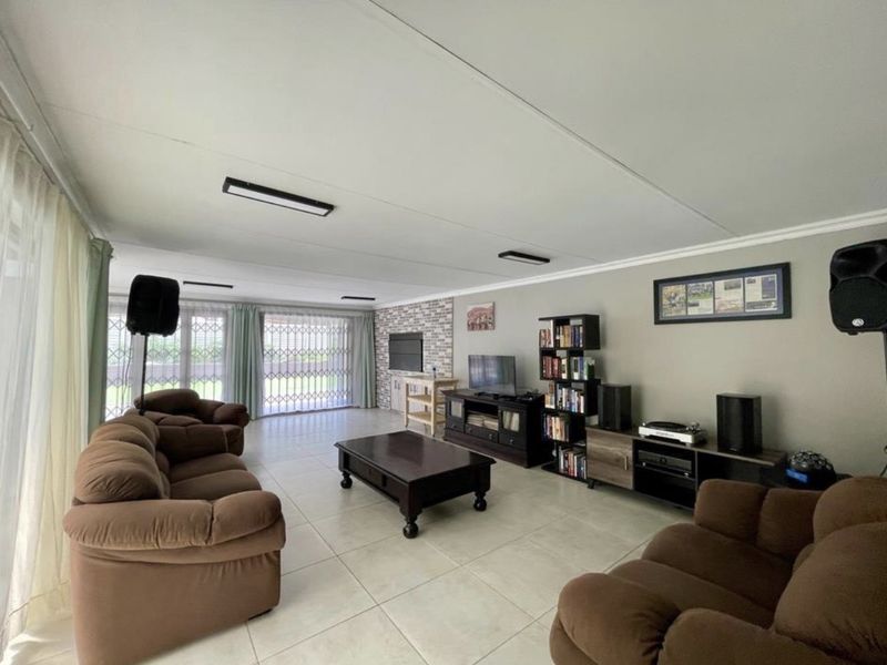Spacious living room featuring large format floor tiles, a brick feature wall, and sliding glass doors with security gates leading to the exterior.