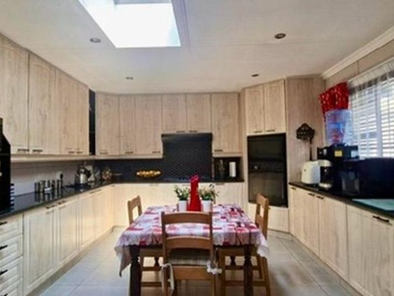 Spacious kitchen featuring light wood cabinetry, integrated appliances, a central dining area, and a skylight providing ample natural light.