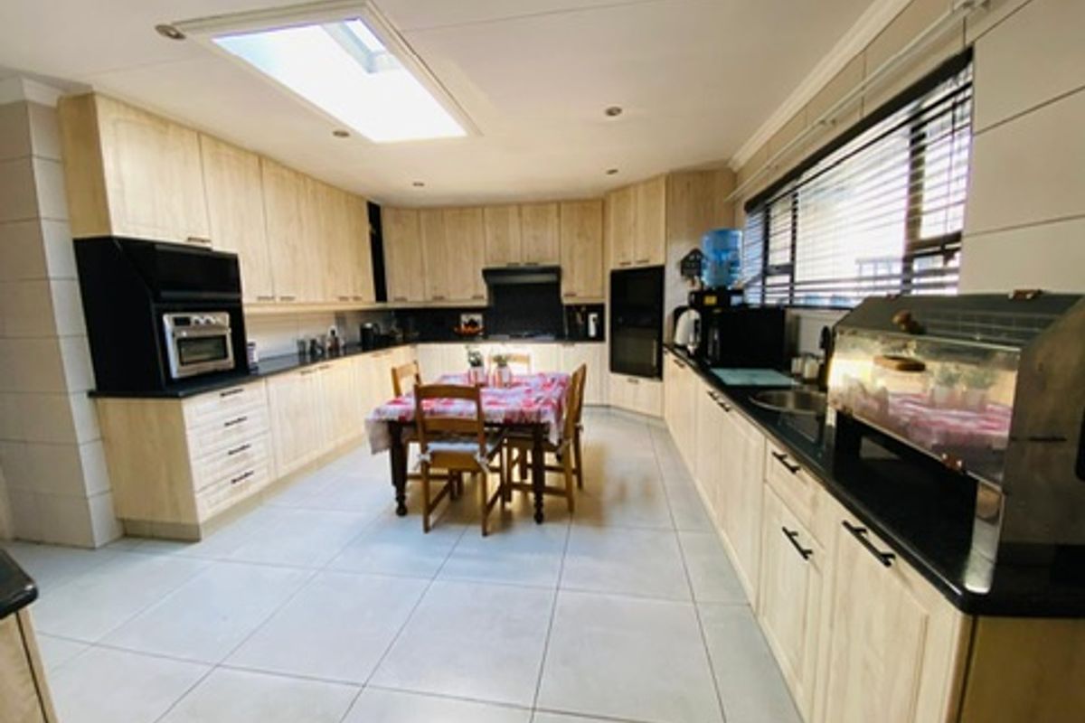 Spacious kitchen featuring light wood cabinetry, dark countertops, tiled flooring, and a skylight, providing a functional layout with ample storage and workspace.