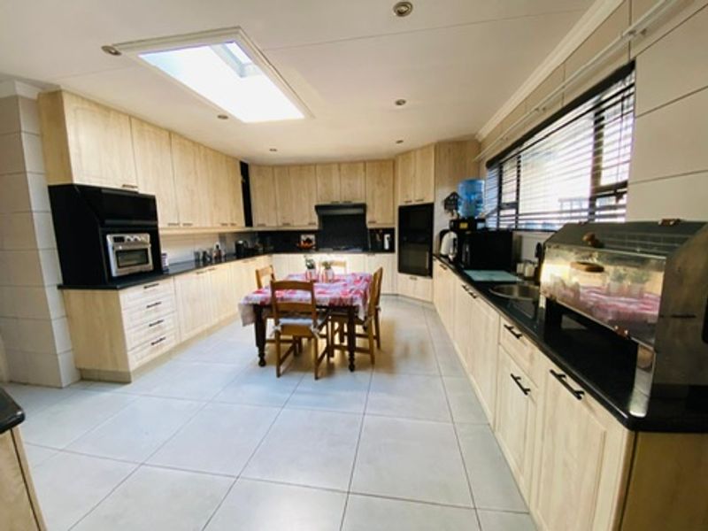 Spacious kitchen featuring light wood cabinetry, dark countertops, tiled flooring, and a skylight, providing a functional layout with ample storage and workspace.